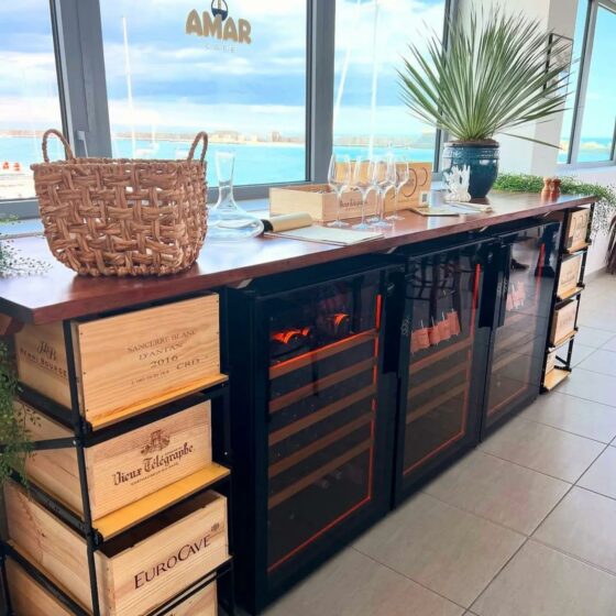 Caves à vin EuroCave basse hauteur installées dans un restaurant en bord de mer, avec bouteilles aux étiquettes ambrées et éclairage orange caractéristique
